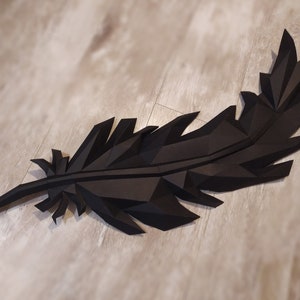 May include: A black paper feather sculpture with a geometric design. The feather is made of folded paper and has a 3D effect.