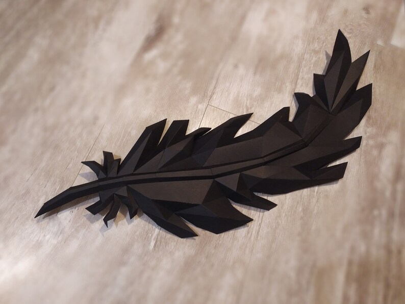 May include: A black paper feather sculpture with a geometric design. The feather is made of folded paper and has a 3D effect.