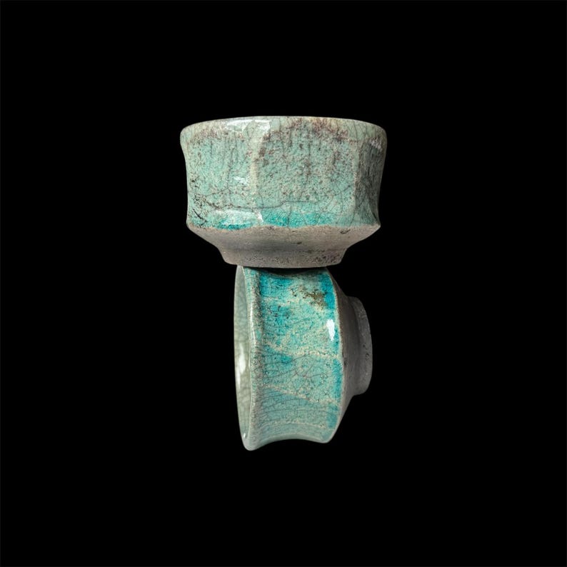 May include: Two teal ceramic teacups with a crackled glaze. The cups are stacked on top of each other.