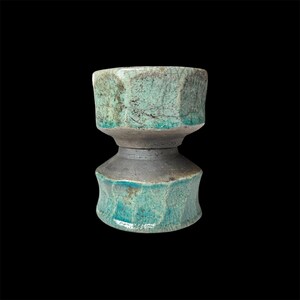 May include: A teal ceramic vase with a textured, crackled glaze. The vase has a unique hourglass shape with two sections.
