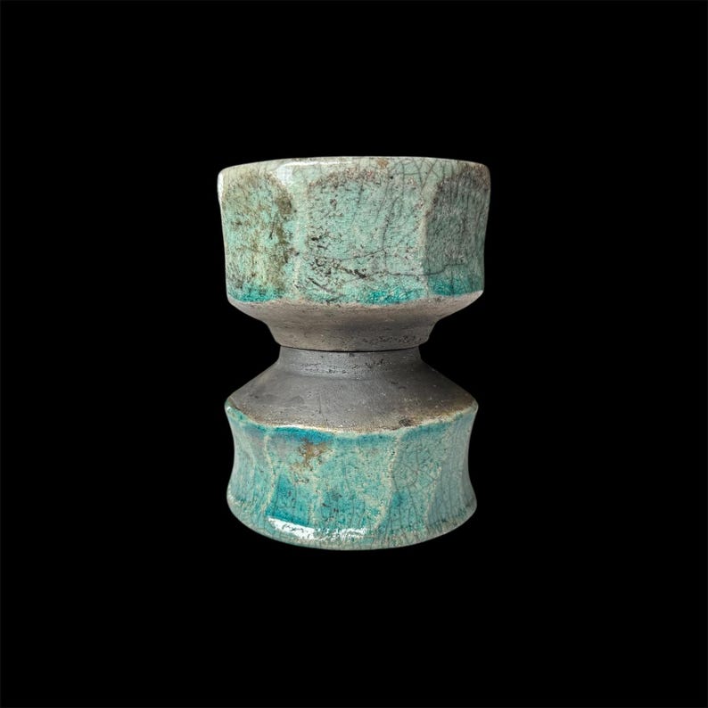 May include: A teal ceramic vase with a textured, crackled glaze. The vase has a unique hourglass shape with two sections.