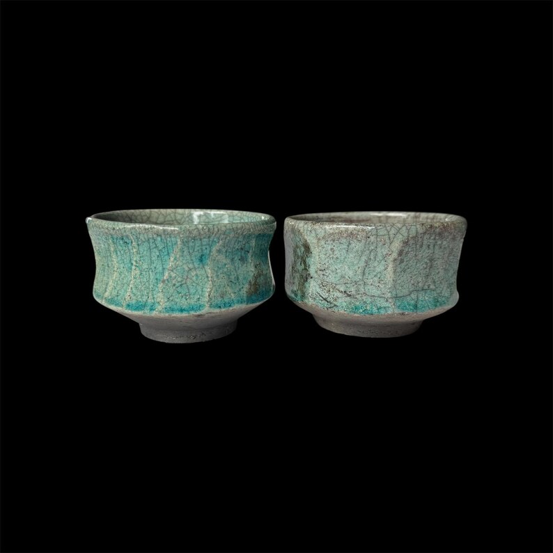 May include: Two small, teal-coloured ceramic bowls with a crackled glaze. The bowls have a rounded shape and a slightly flared rim.