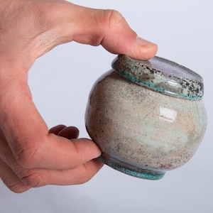 May include: A set of three ceramic mugs with a speckled, matte finish. The mugs are in shades of cream, light gray, and dark gray. Each mug has a simple, minimalist design, perfect for coffee or tea.