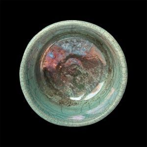 May include: A green ceramic bowl with a crackled glaze and iridescent finish. The bowl is round and has a smooth, glossy surface.