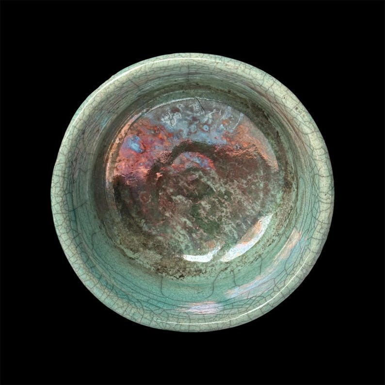 May include: A green ceramic bowl with a crackled glaze and iridescent finish. The bowl is round and has a smooth, glossy surface.