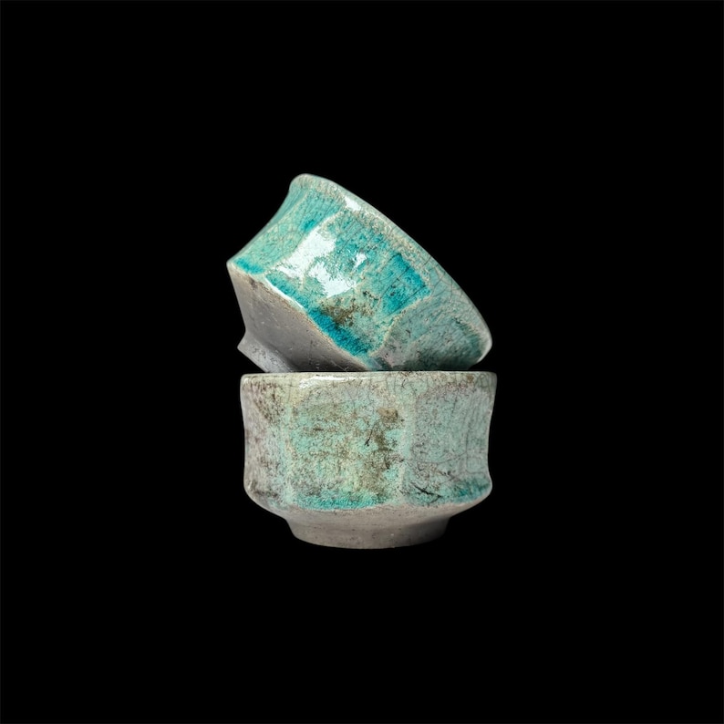 May include: Two stacked ceramic bowls with a teal glaze and a speckled finish. The bowls are slightly misshapen and have a rustic look.