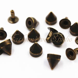May include: A collection of 12 antique gold-toned metal pyramid-shaped studs with a flat back. The studs have a pointed top and a round base.