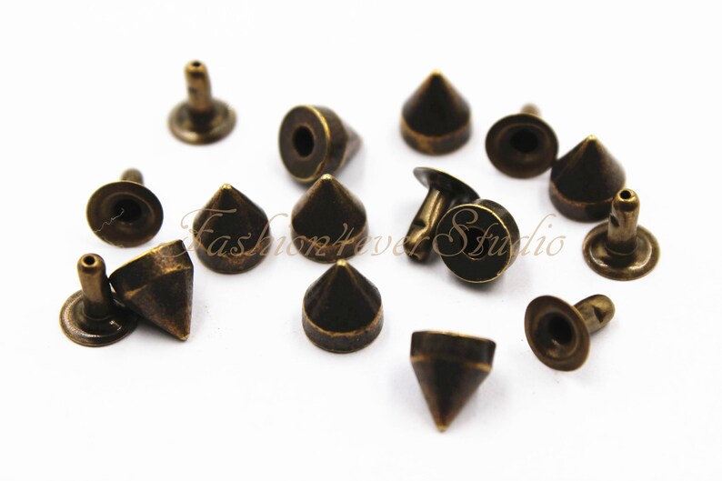 May include: A collection of 12 antique gold-toned metal pyramid-shaped studs with a flat back. The studs have a pointed top and a round base.