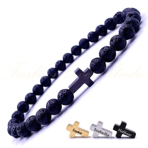Puede incluir: Pulsera de cuentas de roca volcánica negra con un dije de cruz de metal negro. Se muestran tres dijes adicionales con los nombres "Sophia", "Isabella" y "Matthew" grabados en ellos.