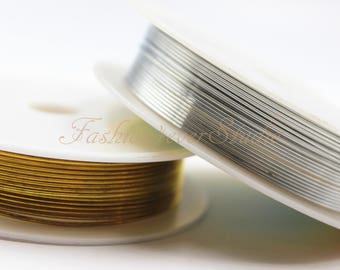 May include: Two spools of wire, one gold and one silver, are wound around white spools. The spools are on a white surface.