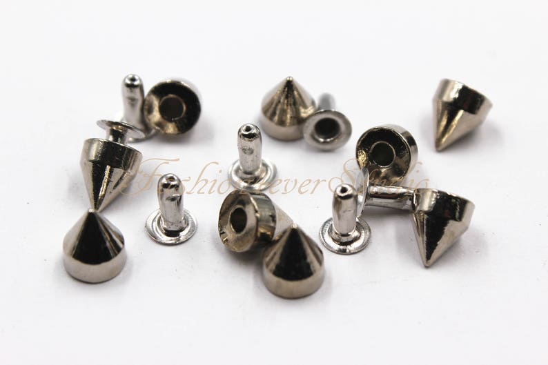 May include: Assortment of silver-toned metal pyramid-shaped studs with a flat back. The studs have a pointed top and a circular base.