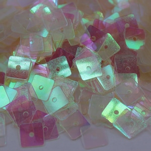 May include: A pile of iridescent square sequins in shades of white, pink, and green. The sequins have a holographic finish and are ideal for crafting and decorating.