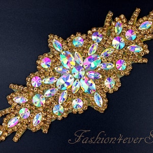 May include: A gold and iridescent rhinestone applique with a floral design. The applique is ideal for adding sparkle to clothing, accessories, or home decor.