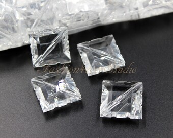 May include: Four clear glass square pyramid-shaped embellishments with a faceted design. The embellishments are on a black surface.