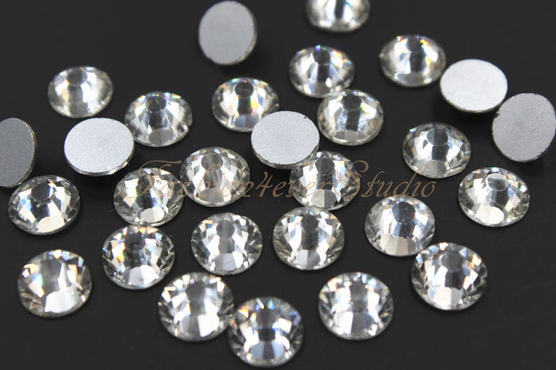 Pu&ograve; includere: Una collezione di strass di vetro trasparente con retro piatto e design sfaccettato. Gli strass sono disposti su una superficie nera.