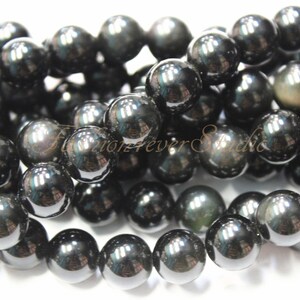 May include: A strand of black obsidian beads with a slight iridescent sheen. The beads are round and smooth, and they are strung on a clear thread.