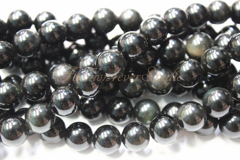 May include: A strand of black obsidian beads with a slight iridescent sheen. The beads are round and smooth, and they are strung on a clear thread.