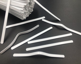 以下が含まれることがあります： 顔面マスク用の白いプラスチック製の鼻ワイヤーの山をクローズアップした写真。ワイヤーは柔軟性があり、鼻の形に合わせて曲げることができます。