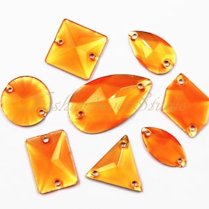 Peut inclure: Assortiment de strass en cristal orange de différentes formes, notamment rondes, ovales, carrées et en forme de goutte. Les strass ont deux trous pour coudre ou fixer.