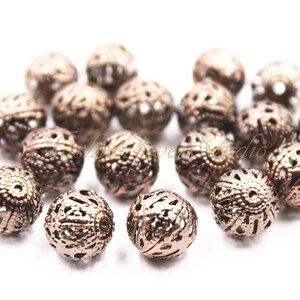 Può includere: Una collezione di perline in metallo color rame con disegni intricati. Le perline sono rotonde e hanno un centro vuoto. Sono perfette per la creazione di gioielli o per l'artigianato.