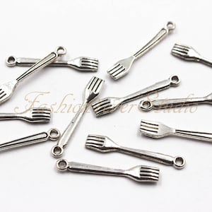 Op de afbeelding: Een groep zilverkleurige metalen vorkcharms met een lus aan de bovenkant om aan sieraden of andere knutselwerken te bevestigen.