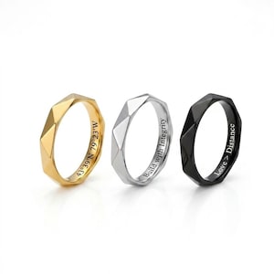May include: Three faceted rings in gold, silver, and black. The gold ring has the coordinates "43°39'N 79°23'W" engraved. The silver ring says "Build with Integrity." The black ring says "Love > Distance."