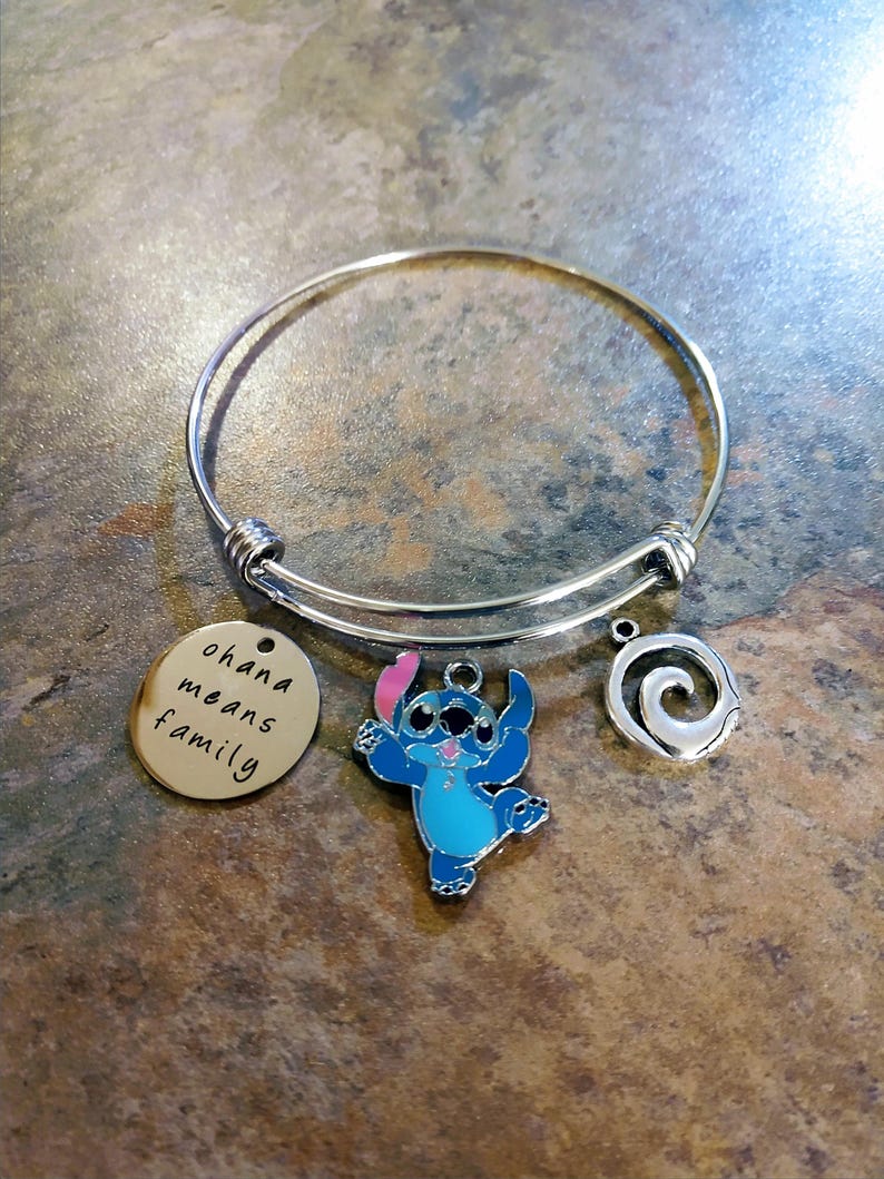 Peut inclure: Un bracelet jonc argent&eacute; avec trois breloques. Une breloque est un disque dor&eacute; avec l'inscription "ohana means family". Les autres breloques sont un personnage de dessin anim&eacute; bleu et une spirale argent&eacute;e.