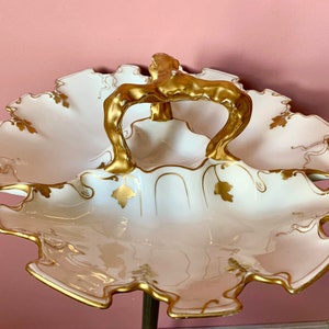 以下が含まれることがあります： 金色の取っ手と金箔のアクセントが付いた白い磁器製のサービングディッシュ。ディッシュは3つのセクションに分かれており、波状のエッジでデザインされています。