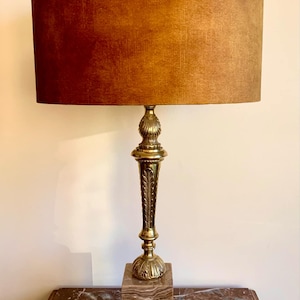 Op de afbeelding: Een messing tafellamp met een bruine fluwelen lampenkap. De lamp heeft een vierkante voet van marmer met sierlijke details.
