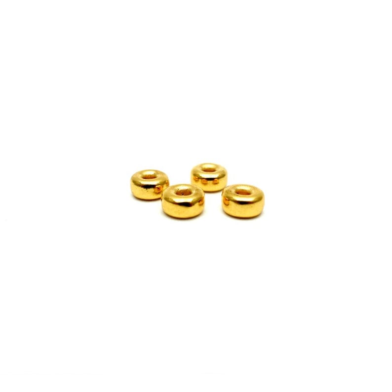 May include: Four gold-colored metal beads with a round hole in the center. The beads are arranged in a row on a white background.