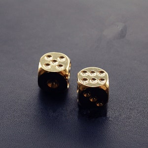 May include: Two gold metal dice with black spots on each side. The dice are on a dark blue surface.