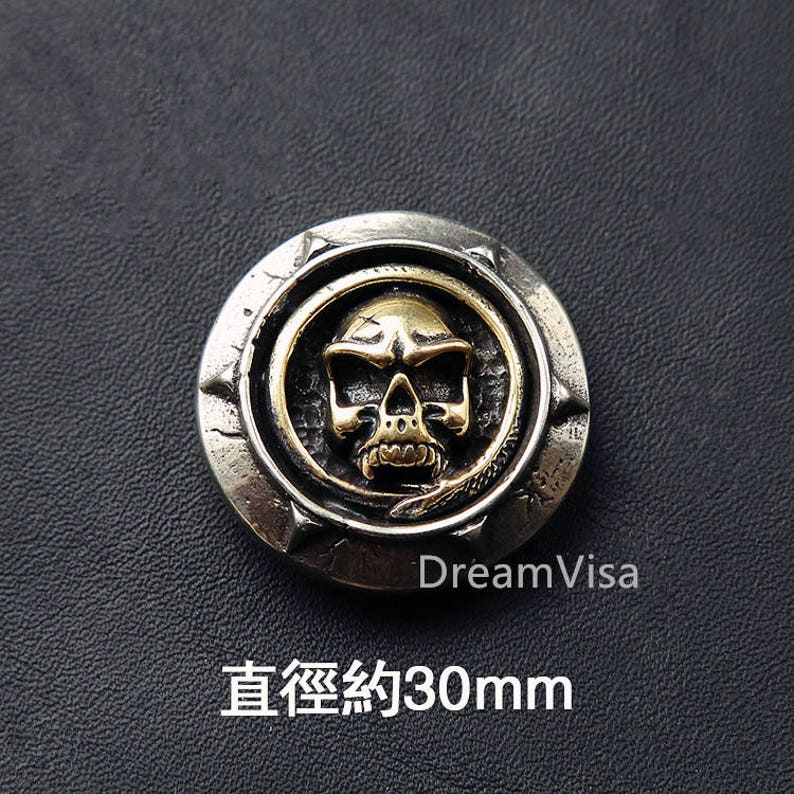 May include: A silver and gold skull button with a snake design. The button is approximately 30mm in diameter.