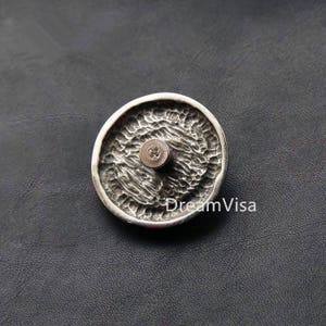 May include: A silver-toned round button with a textured surface and a screw in the center.