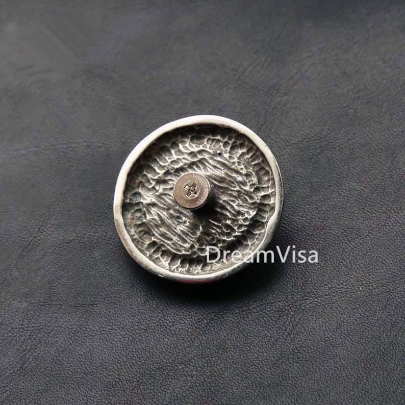 May include: A silver-toned round button with a textured surface and a screw in the center.