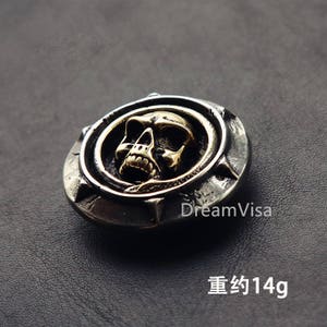 May include: A silver and gold skull pendant with a snake design. The pendant weighs approximately 14 grams.