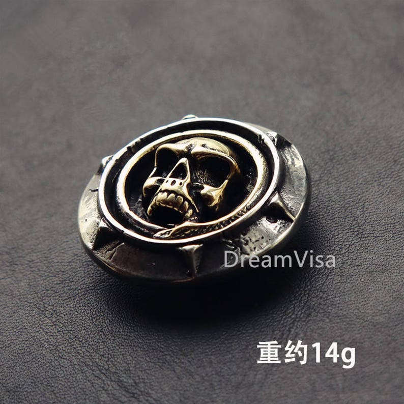 May include: A silver and gold skull pendant with a snake design. The pendant weighs approximately 14 grams.