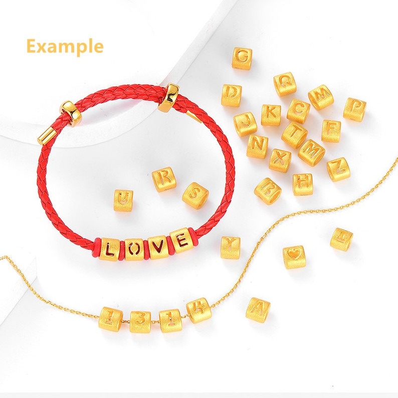May include: A red string bracelet with gold letter beads spelling "LOVE".  The bracelet is surrounded by loose gold letter beads, including the letters A, B, C, D, E, F, G, H, I, J, K, L, M, N, O, P, Q, R, S, T, U, V, W, X, Y, and Z.  There is also a gold chain with gold number beads spelling "1314".