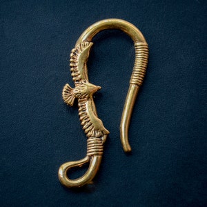 Puede incluir: Un gancho de metal dorado con un diseño de pájaro. El gancho tiene forma de pájaro en vuelo, con las alas extendidas. El gancho está hecho de un metal grueso y resistente y tiene un acabado liso.