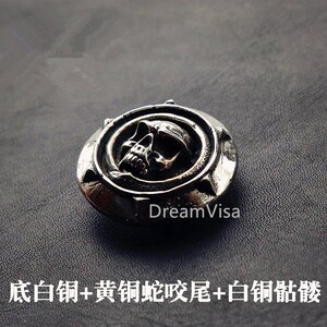 May include: A silver skull pendant with a detailed design. The skull is surrounded by a circle with a starburst pattern. The pendant is on a dark gray background.