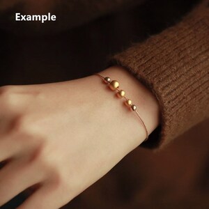 K&ouml;nnte beinhalten: Ein zartes goldenes Armband mit einer Kette und einer Reihe von abgestuften goldenen Perlen.