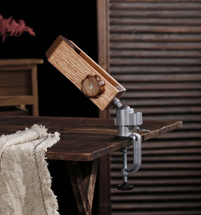 K&ouml;nnte beinhalten: Eine Holz-Klemme mit einer Metallbasis und einem Knopf zum Festziehen. Die Klemme ist auf einem Holztisch montiert.