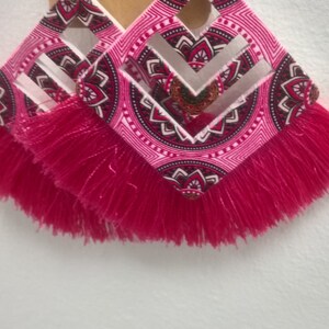 May include: A pair of pink and white geometric patterned earrings with pink fringe tassels.