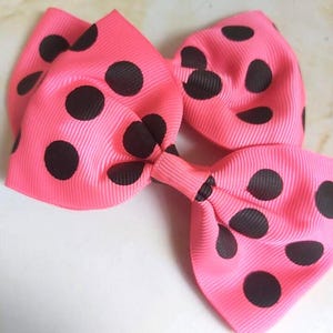Può includere: Un fiocco rosa acceso con grandi pois neri. Il fiocco è realizzato in tessuto a coste ed è annodato al centro. Questo accessorio è perfetto per aggiungere un tocco di colore a qualsiasi outfit.