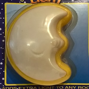 Puede incluir: Una luz táctil en forma de media luna amarilla, que funciona con pilas. El embalaje dice "Touch Light" y "Solo presiona para encender".