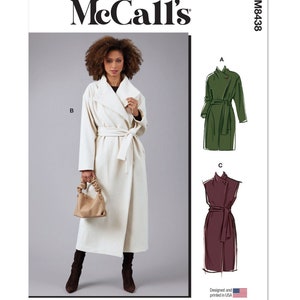 May include: A woman models a cream-colored wrap coat with a matching belt. The McCall's pattern M8438 is displayed, showing illustrations of the coat in green and burgundy. The pattern is designed and printed in the USA.