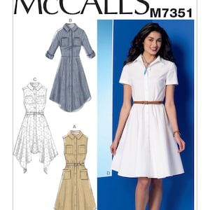 May include: McCall's M7351 sewing pattern featuring four shirt dress designs. The image shows a woman wearing a white dress with a brown belt. The pattern includes options for sleeveless, short-sleeved, and long-sleeved dresses. The text on the pattern reads "Separate cup size pattern pieces for Misses: A/B, C, D."