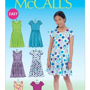 May include: McCall's sewing pattern for girls' dresses. The image shows a young girl wearing a floral print dress. The pattern includes several dress designs in various colors and patterns, including green, blue, purple, and pink. The word "EASY" is in a pink circle.
