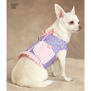 May include: A white Chihuahua dog wearing a blue floral print dog dress with pink accents. The dress features a pink gingham pocket, lace trim, and a pink bow. The text "Simplicity Pattern 2393" is visible.