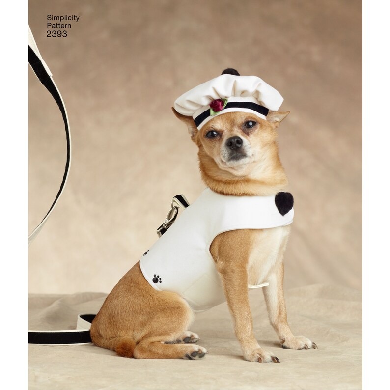 May include: A small dog wearing a white chef's hat with a black band and a red rose, and a matching white vest with a black heart and paw print. The dog is sitting and looking at the camera. The text "Simplicity Pattern 2393" is in the upper left corner.