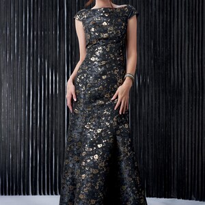 May include: A long, black and gold dress with a floral pattern. The dress has a boat neck and short sleeves. It is fitted through the bodice and flares out at the skirt.